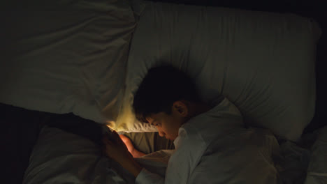 Young-Boy-In-Bedroom-At-Home-Lying-In-Bed-Using-Mobile-Phone-To-Text-Message-At-Night